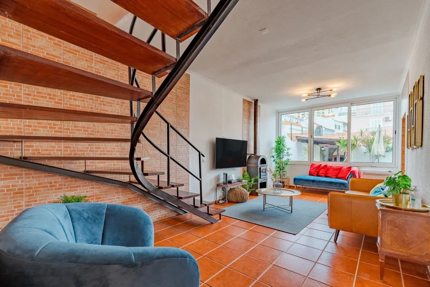 Renovated two-storey living room in Vila das Fontaínhas, Setúbal, with exposed brick, a spiral steel stair and terracotta floor